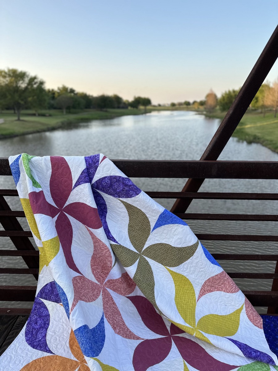 A colorful pinwheel quilt draped over a bridge railing at golden hour